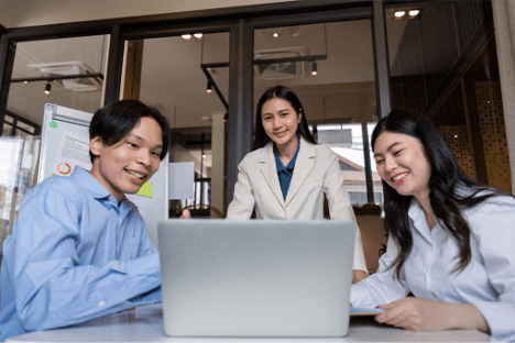 Three individuals collaborating in front of a laptop showing eagerness to work.